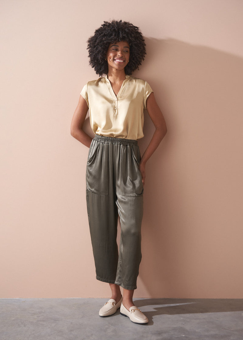 Woman wearing a light yellow satin blouse and green satin trousers against a beige background