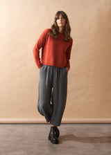Woman wearing a red sweater and checkered pants against a beige wall.