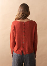 Person wearing a red cardigan with buttons on a beige background