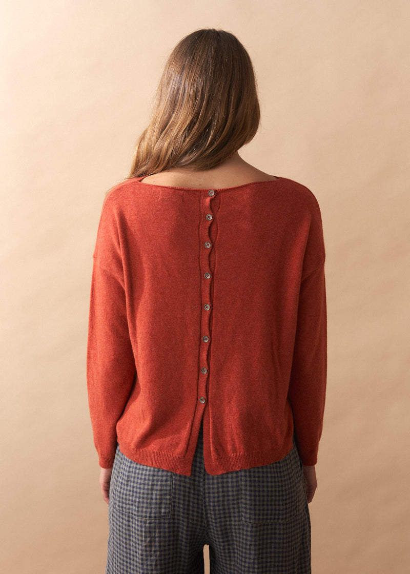 Person wearing a red cardigan with buttons on a beige background