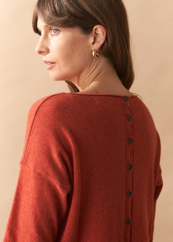 Woman wearing a rust-colored cardigan with black buttons on a beige background