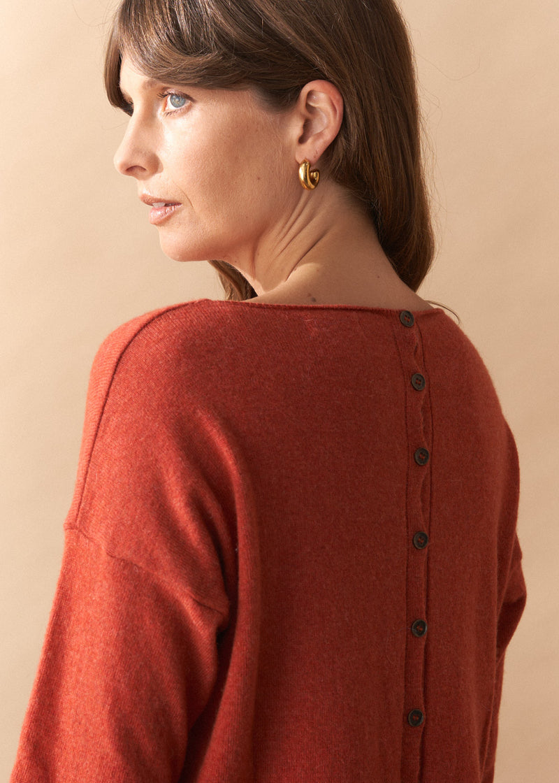 Woman wearing a rust-colored cardigan with black buttons on a beige background