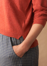 Person wearing a red sweater and blue checkered pants against a beige background