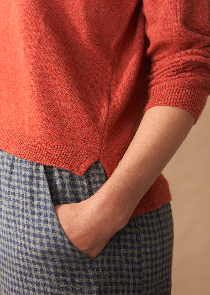 Person wearing a red sweater and blue checkered pants against a beige background