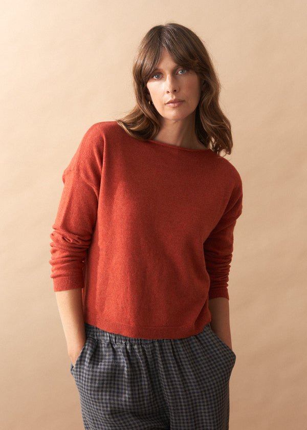 Woman wearing a red sweater and plaid pants against a beige background