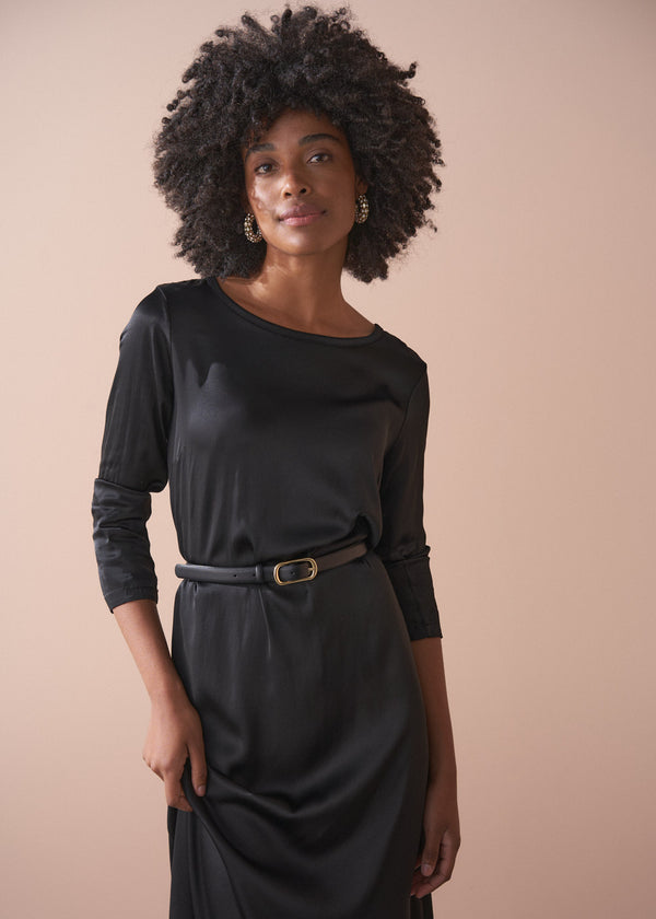 Woman wearing a black satin dress standing against a beige background