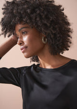 Woman wearing a black satin dress standing against a beige background