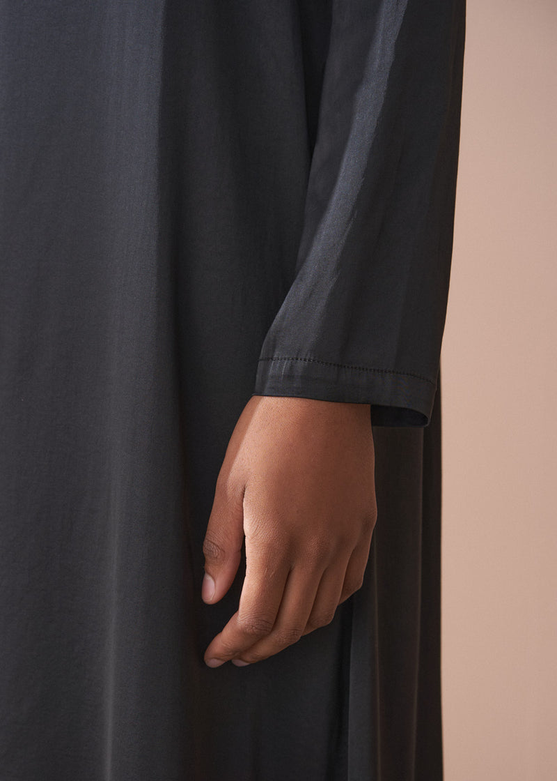 Woman wearing a black satin dress standing against a beige background