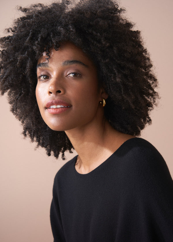 Woman with an afro wearing a black top against a beige background