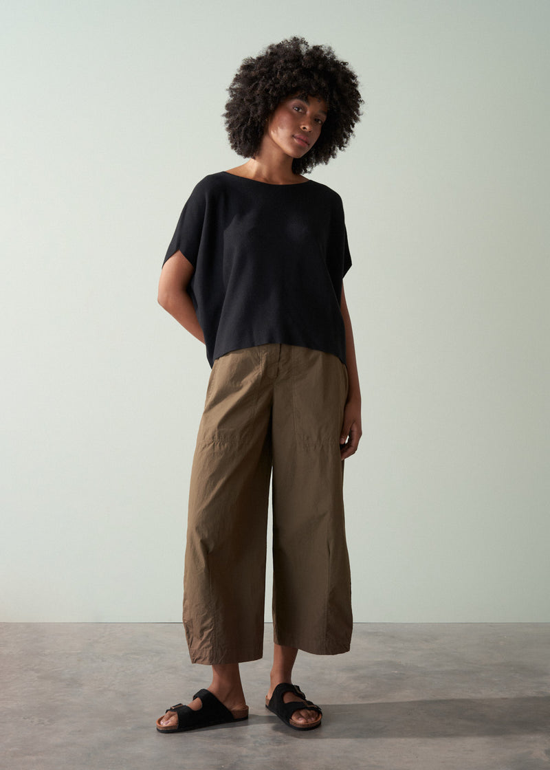 Woman wearing a black top and brown pants against a plain background