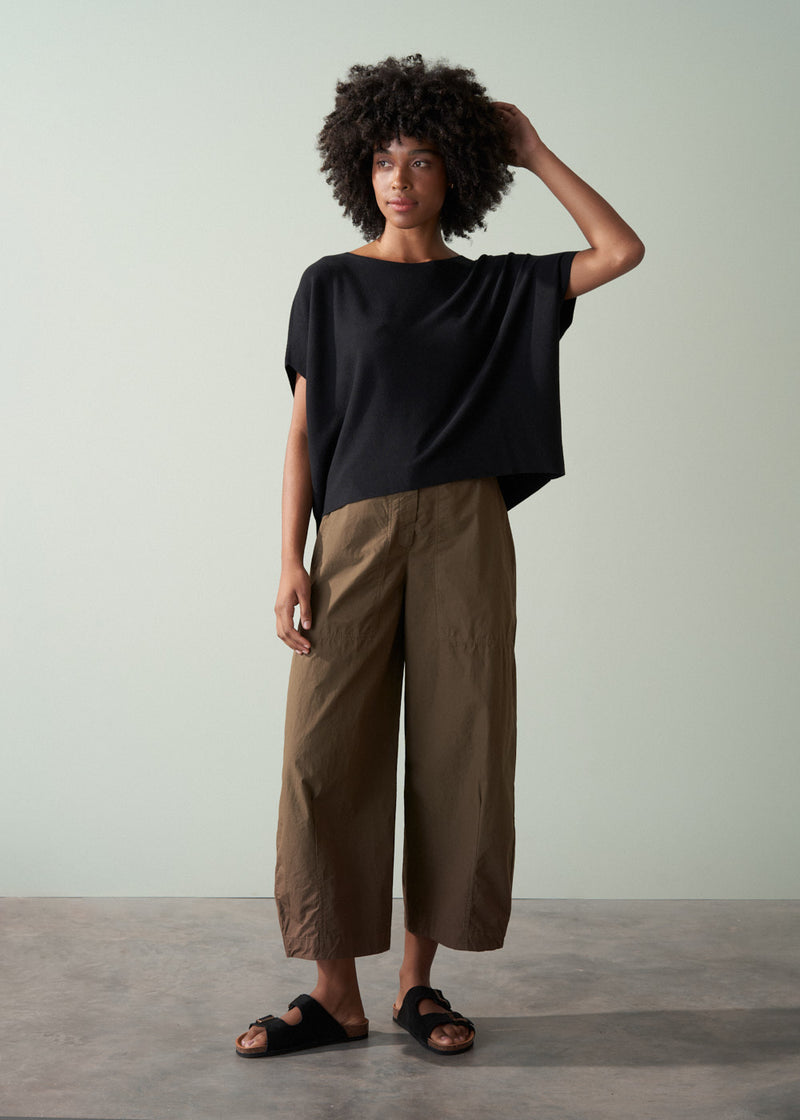 Woman wearing a black top and brown pants against a plain background