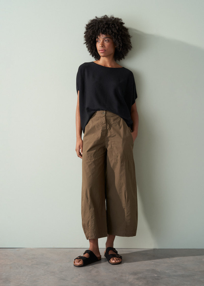 Person wearing a black top and brown wide-leg pants against a white wall.