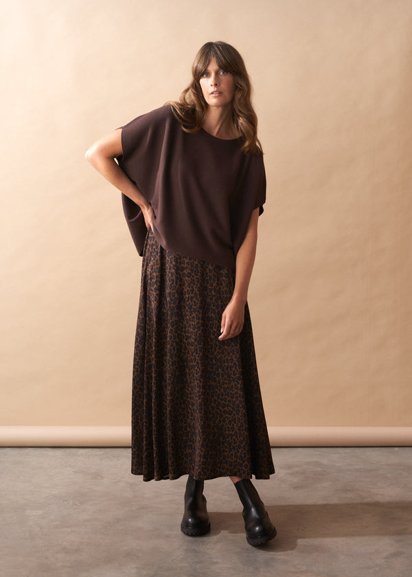 Woman wearing a brown short sleeve knit top against a beige wall