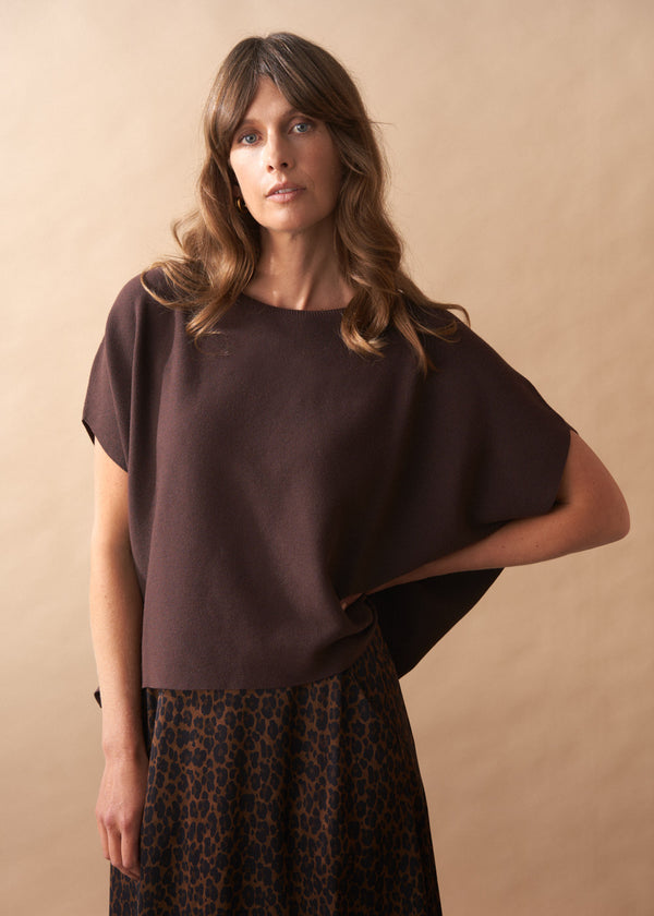 Woman wearing a brown short sleeve knit top with a beige background