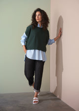 Woman wearing dark green short sleeve knit sweater with leopard print trousers against a plain background.