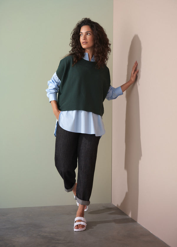 Woman wearing dark green short sleeve knit sweater with leopard print trousers against a plain background.