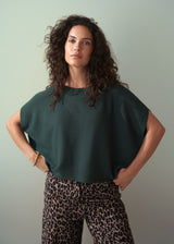 Woman wearing dark green short sleeve knit sweater with leopard print trousers against a plain background.