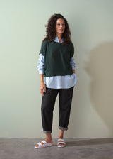 Woman wearing dark green short sleeve knit sweater with leopard print trousers against a plain background.