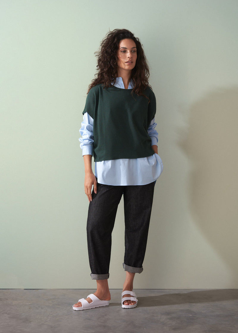 Woman wearing dark green short sleeve knit sweater with leopard print trousers against a plain background.