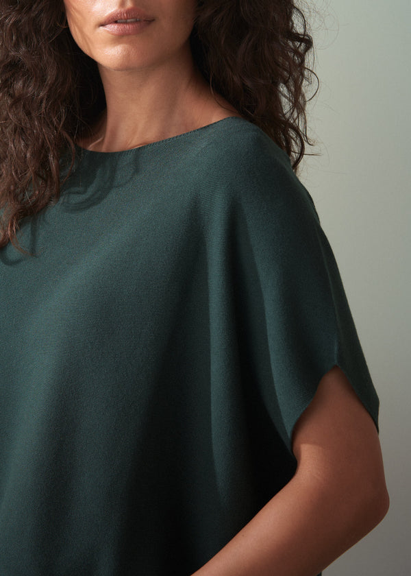 Woman wearing dark green short sleeve knit sweater with leopard print trousers against a plain background.
