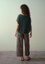 Woman wearing dark green short sleeve knit sweater with leopard print trousers against a plain background.