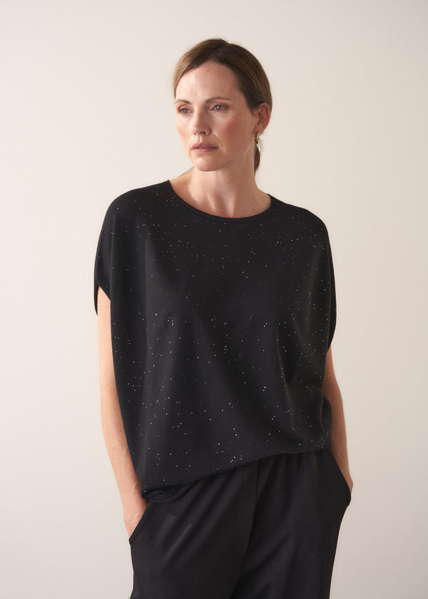 Woman wearing a black top with subtle sequin detail against a plain background