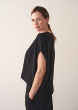 Woman wearing a black top with sequin detail and short sleeves against a plain background
