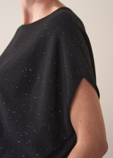 Black top with sequin detail worn by a person, on a neutral background