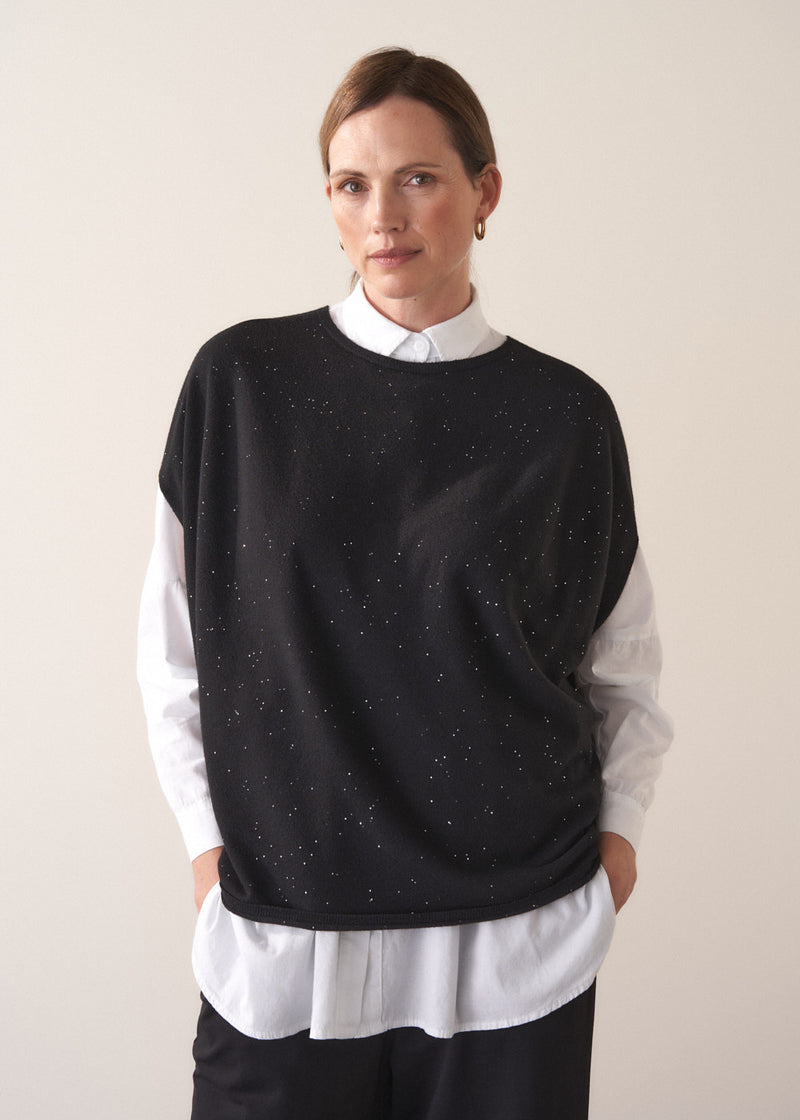 Woman wearing a black sequin detail  sweater over a white shirt on a plain background