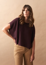 Woman wearing a burgundy knit top and camel wide leg trousers against a beige background