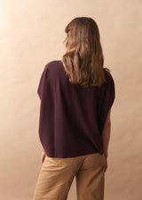 Person wearing a dark purple top and beige pants against a beige background