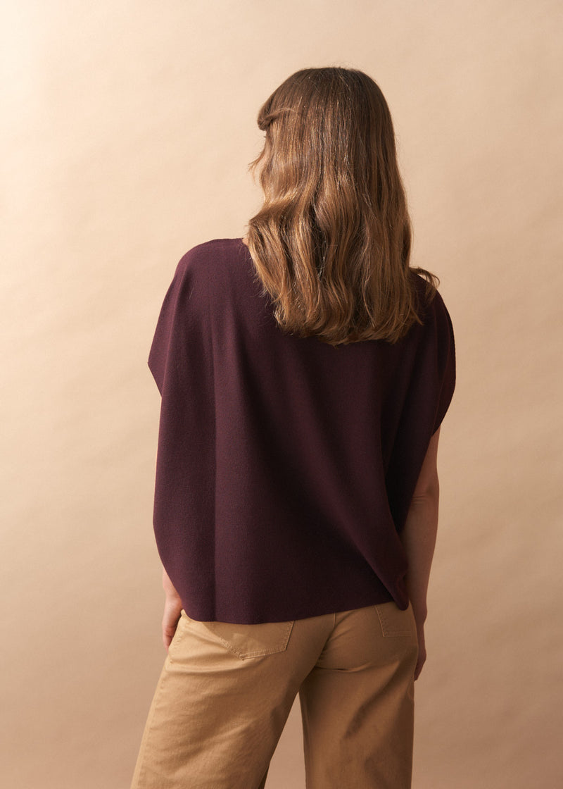 Person wearing a dark purple top and beige pants against a beige background