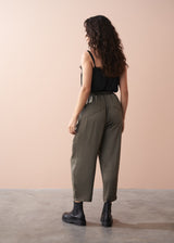 Woman wearing a black camisole top and olive green satin trousers against a beige background
