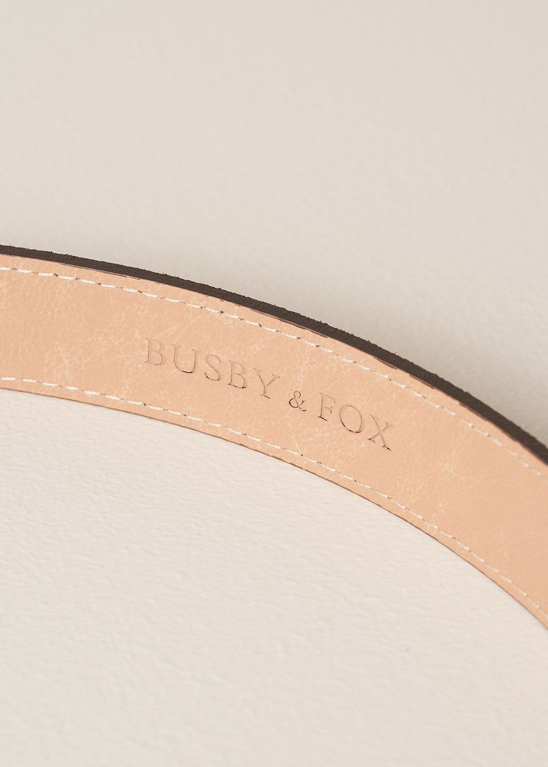 Close-up of a beige leather strap with 'BUSBY & FOX' branding on a light background.