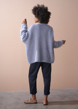 Back of woman wearing a dusky lavender chunky oversized knit cardigan, with blue trousers.