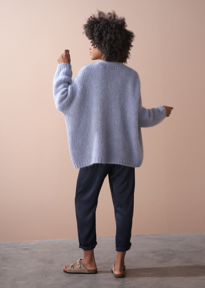 Back of woman wearing a dusky lavender chunky oversized knit cardigan, with blue trousers.