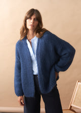 Woman wearing a blue chunky knit cardigan against a beige background.