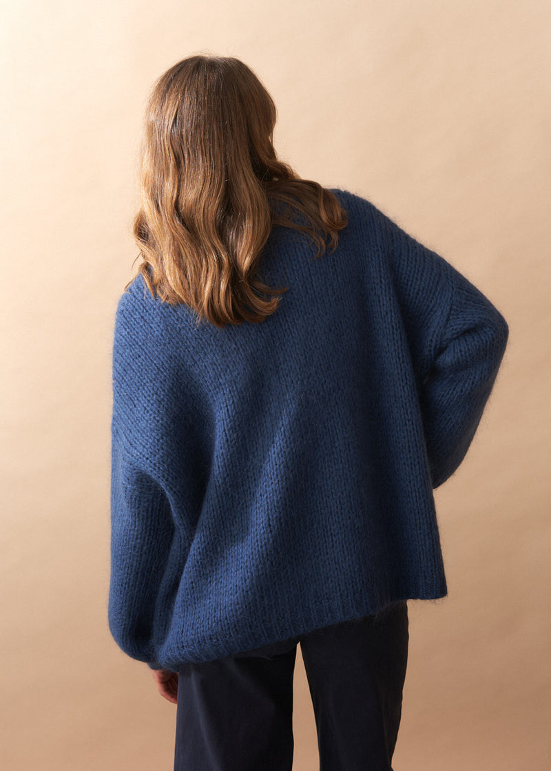 Person wearing a chunky knit blue sweater against a beige background.