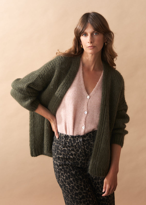 Woman wearing a green cardigan over a pink top and leopard print pants against a beige background