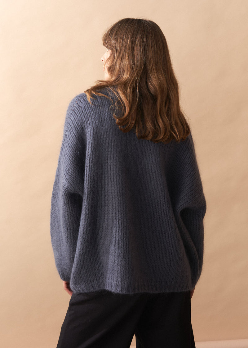 Person wearing a slate grey chunky knit cardigan against a beige background