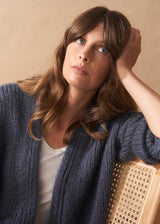 Woman wearing a slate grey chunky knit cardigan with a beige background