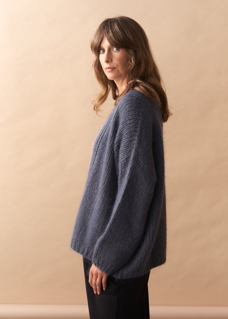 Woman wearing a slate grey chunky knitted cardigan against a beige background