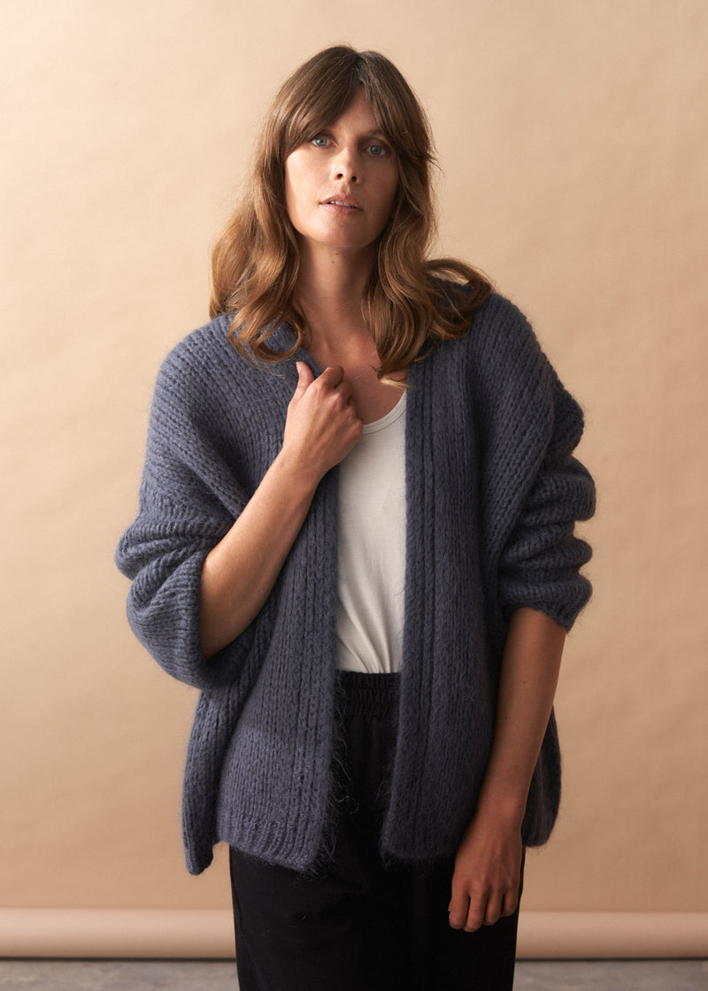 Woman wearing a slate grey chunky knitted cardigan against a beige background