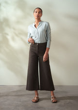 Woman wearing a light blue shirt and brown wide-leg cropped trousers against a neutral background