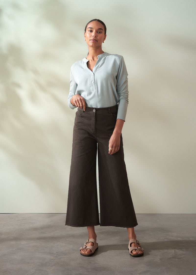 Woman wearing a light blue shirt and brown wide-leg cropped trousers against a neutral background