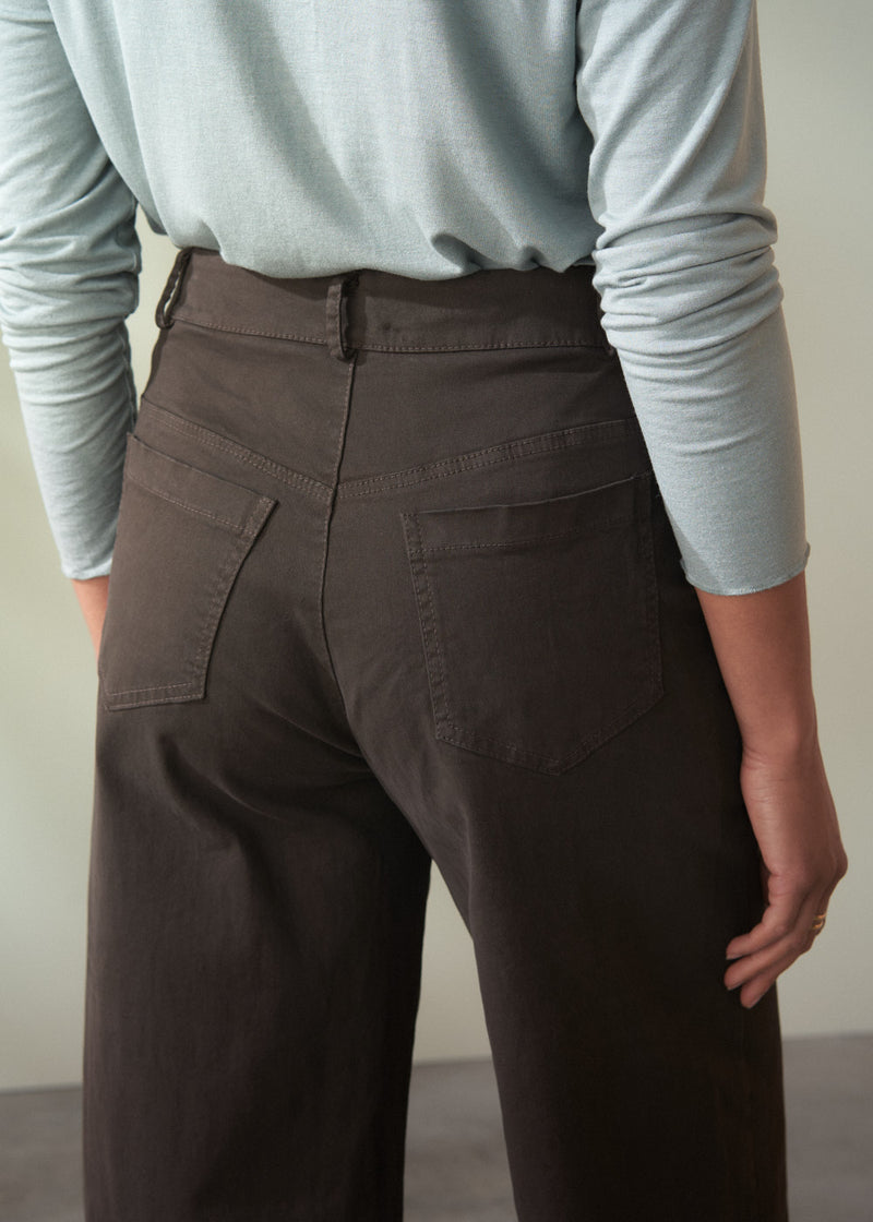 Person wearing brown cropped trousers  and a light blue long-sleeve shirt against a neutral background