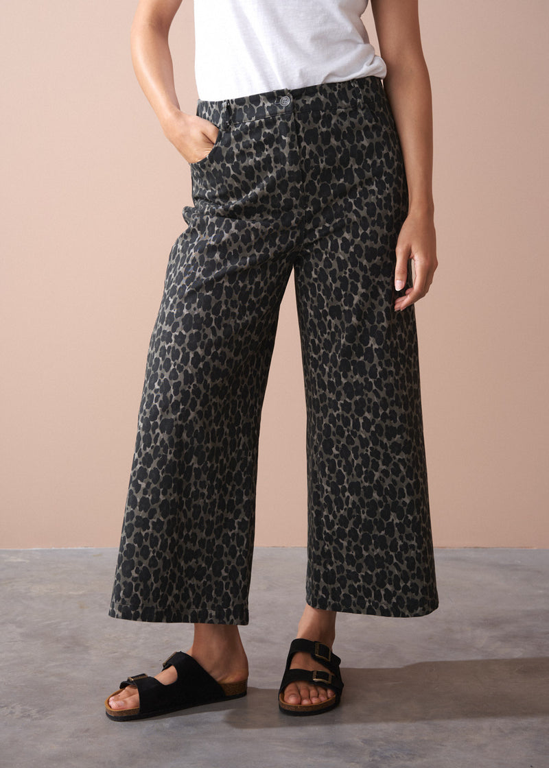 Person wearing khaki leopard print wide leg trousers on a beige background