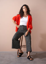 Woman wearing a red cardigan, white top, and khaki leopard print wide leg trousers on a beige background