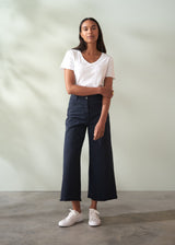 Woman wearing a white t-shirt and dark blue wide leg trousers against a plain background