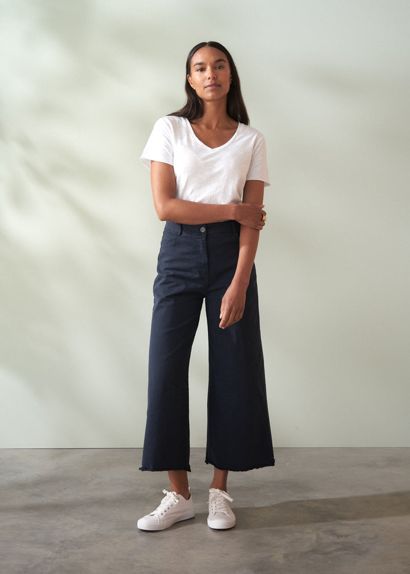 Woman wearing a white t-shirt and dark blue wide leg trousers against a plain background
